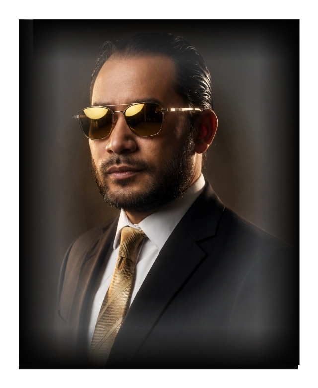 Eden Legacy founder portrait for Midnight Legacy Extrait de Parfum, showing a man in a black suit, gold tie and sunglasses.